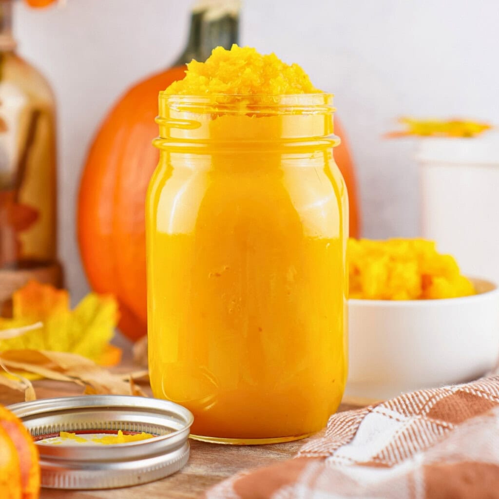 A glass jar of homemade pumpkin puree, surrounded by fresh orange pumpkins.