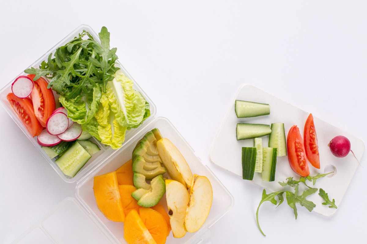 Sliced veggies and fruit in containers on a white background.