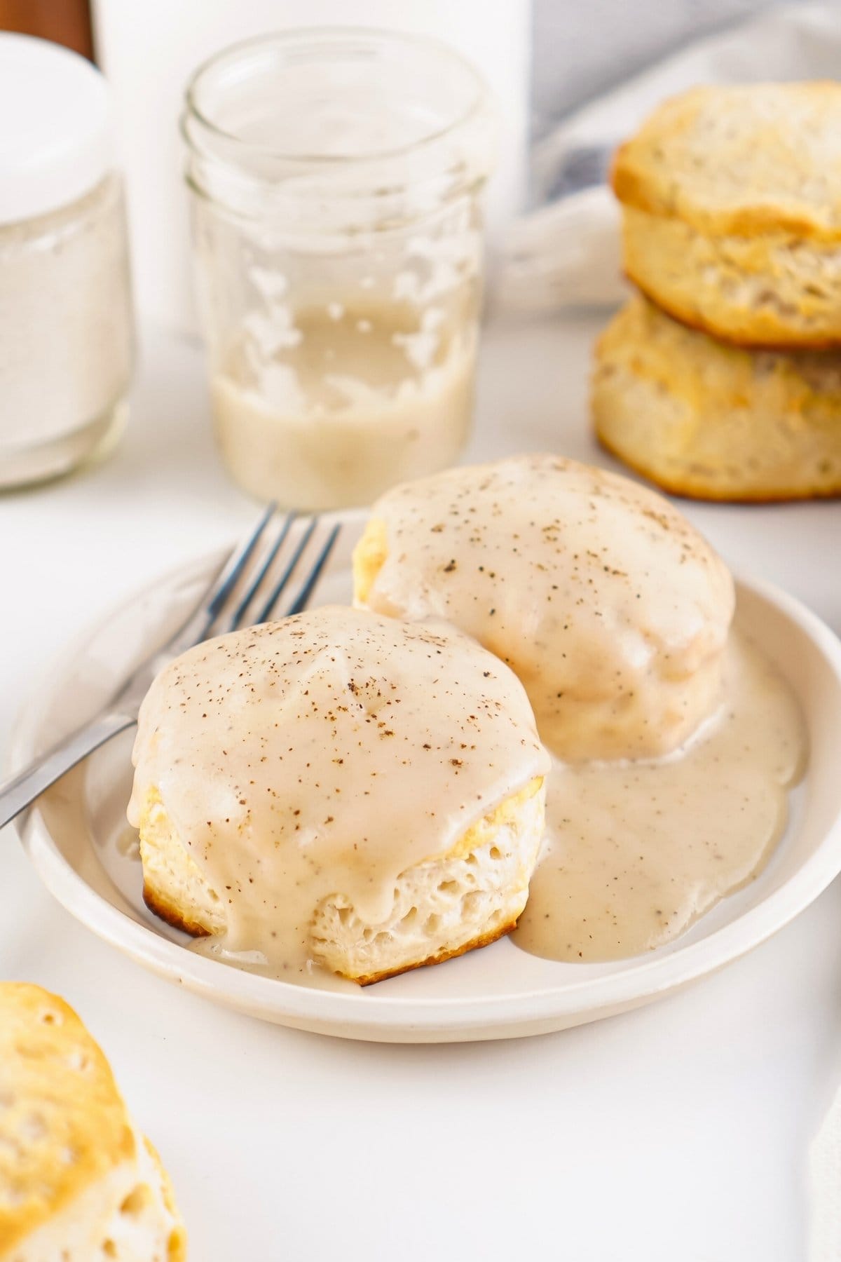 Two biscuits covered in creamy gravy on a plate with a fork nearby.