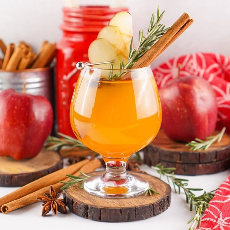 Glass of Fireball Apple Cider with apple slices, cinnamon stick, and rosemary.