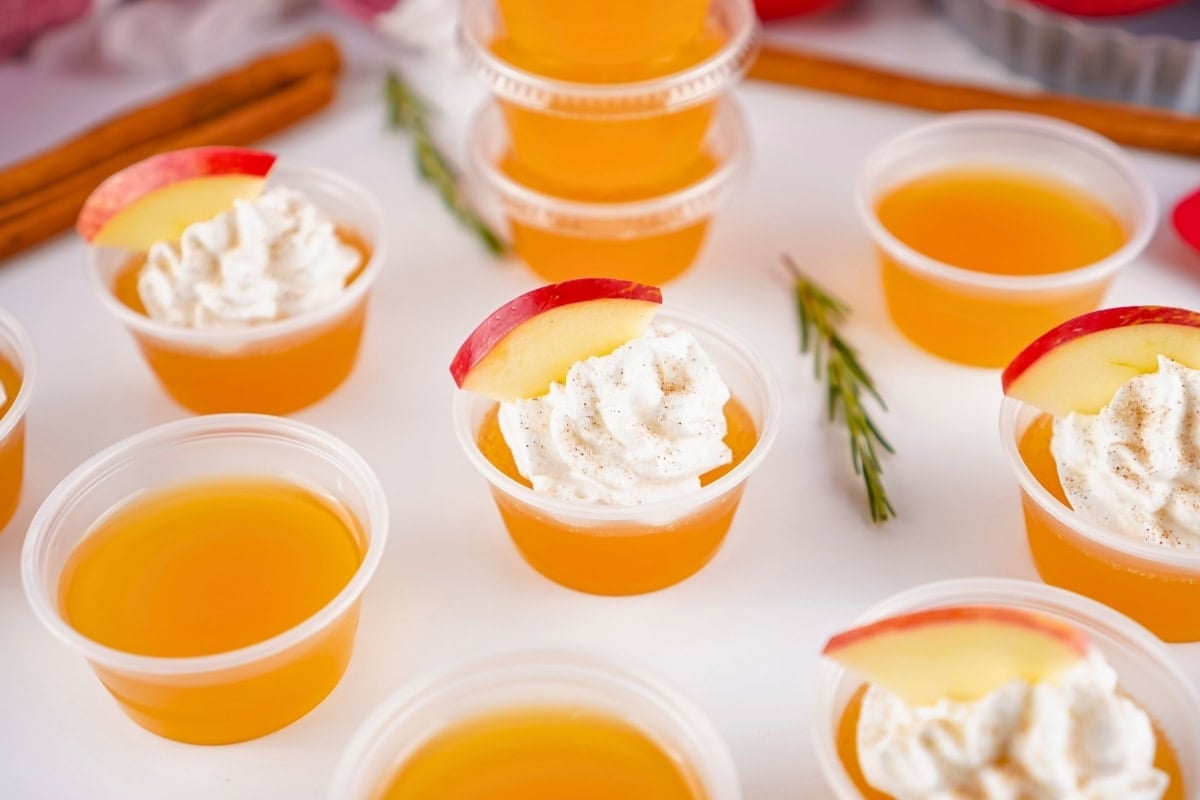 Small cups of orange gelatin, some topped with whipped cream and apple slices.