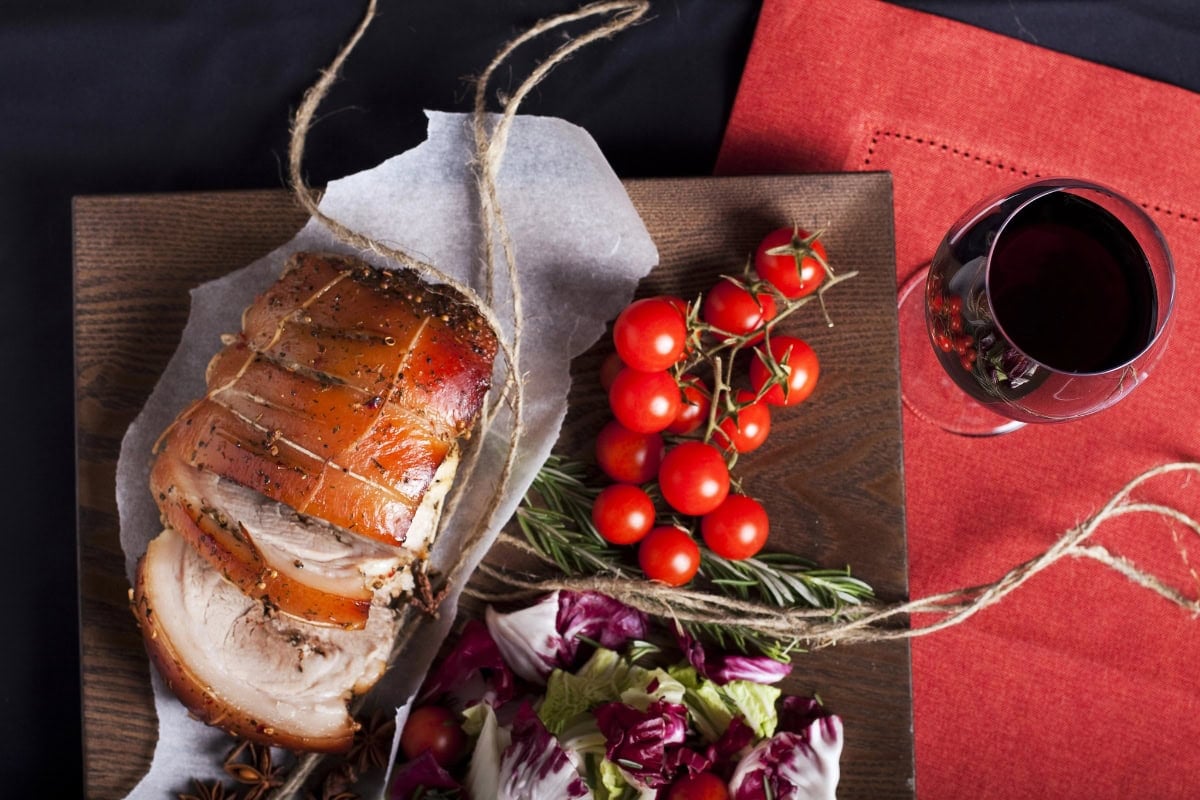 Sliced roast pork, cherry tomatoes, salad, and red wine on a wooden board.