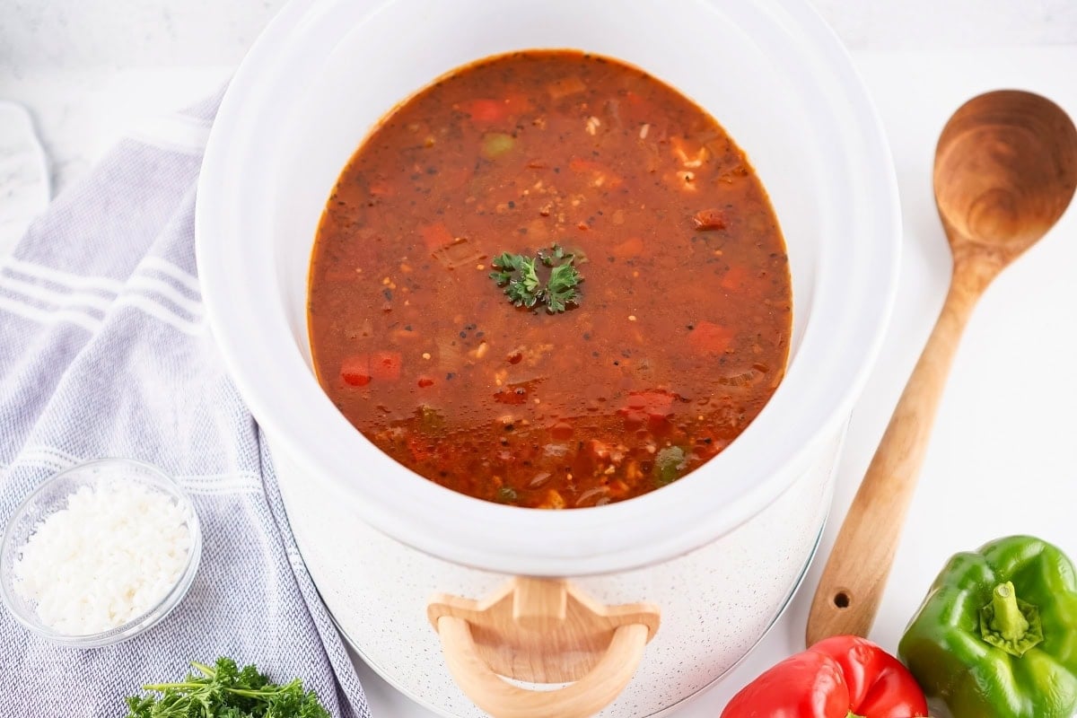 A pot of Stuffed Pepper Soup garnished with parsley, beside peppers and a wooden spoon.
