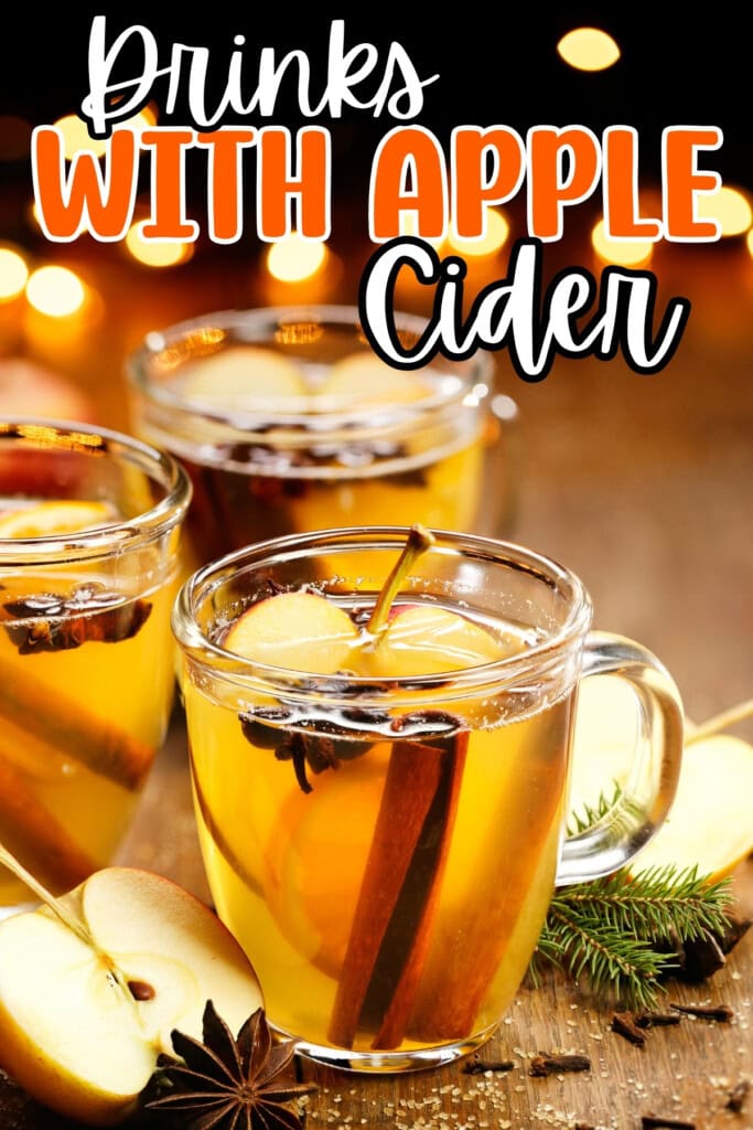 Clear glass mugs of apple cider with cinnamon sticks and apple slices, festive lights.