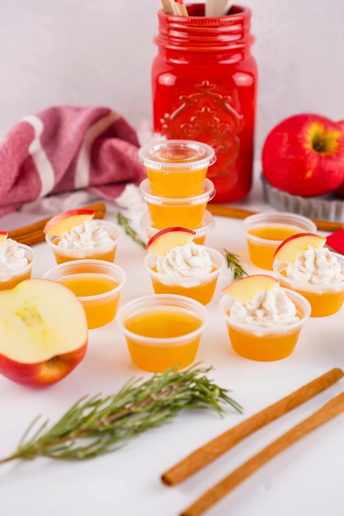 Apple cider gelatin shots with whipped cream, cinnamon sticks, apples, and rosemary.
