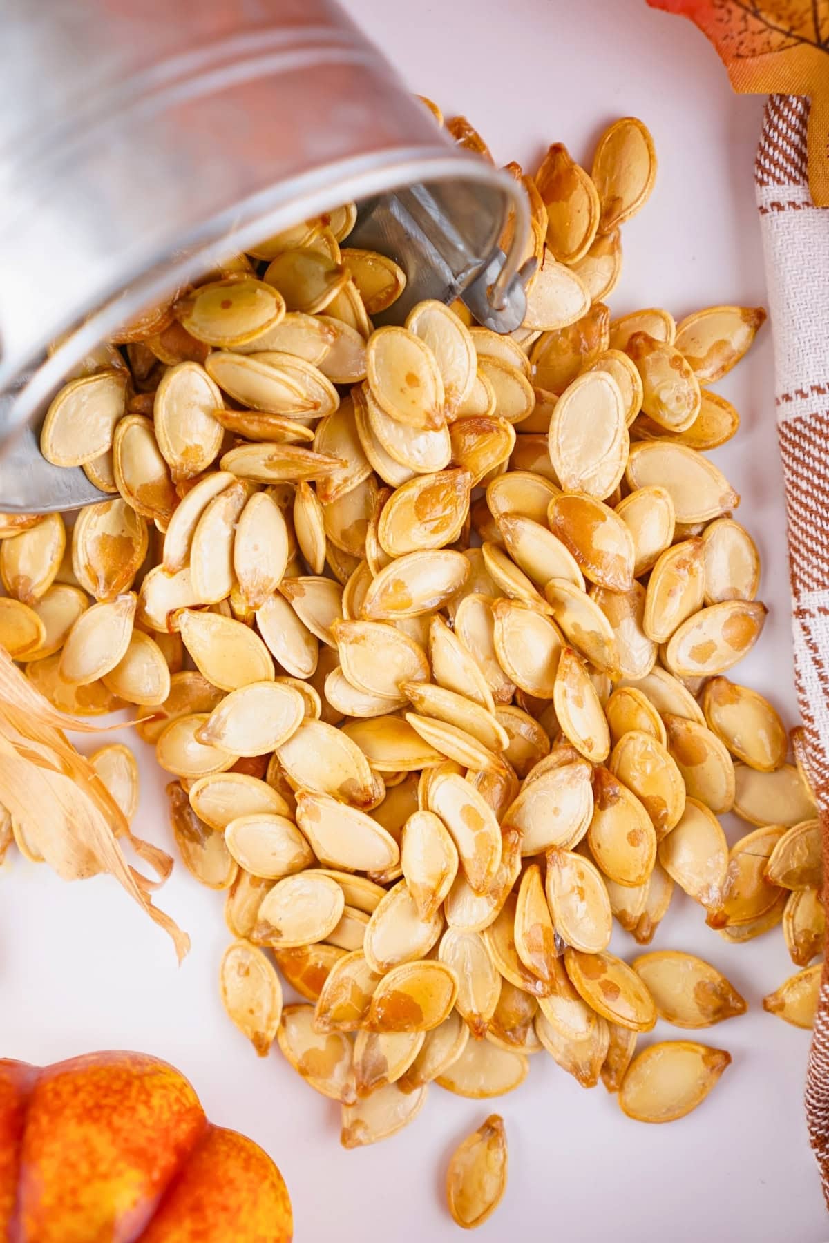 Roasted pumpkin seeds spilling from a metal container onto a white surface.