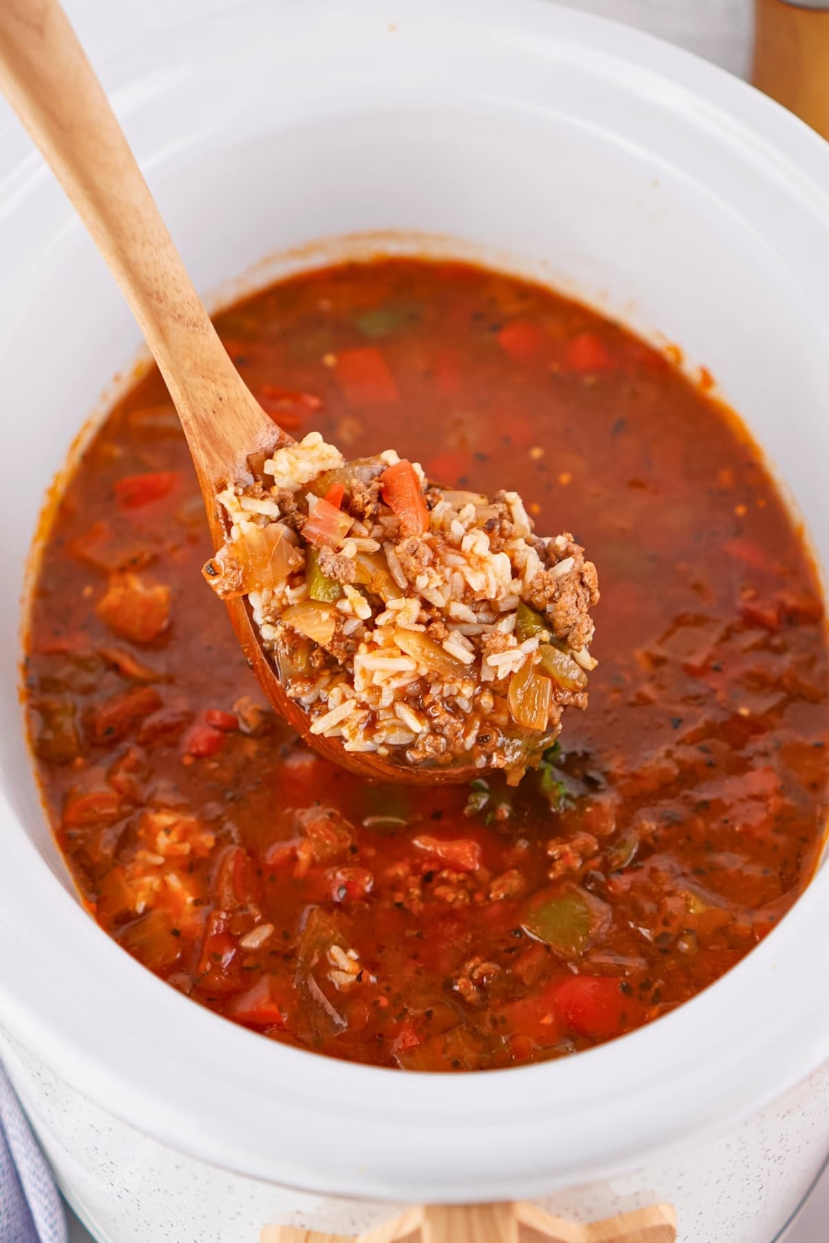A wooden spoon holds a scoop of Stuffed Pepper Soup over a white pot.