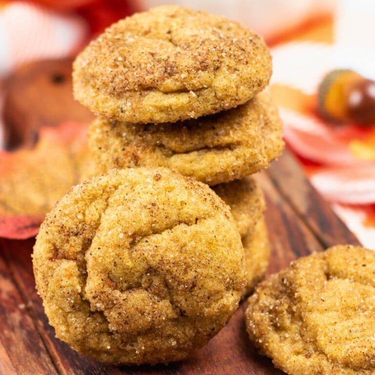 Stack of cinnamon sugar cookies on a wooden board with autumn decor in background.