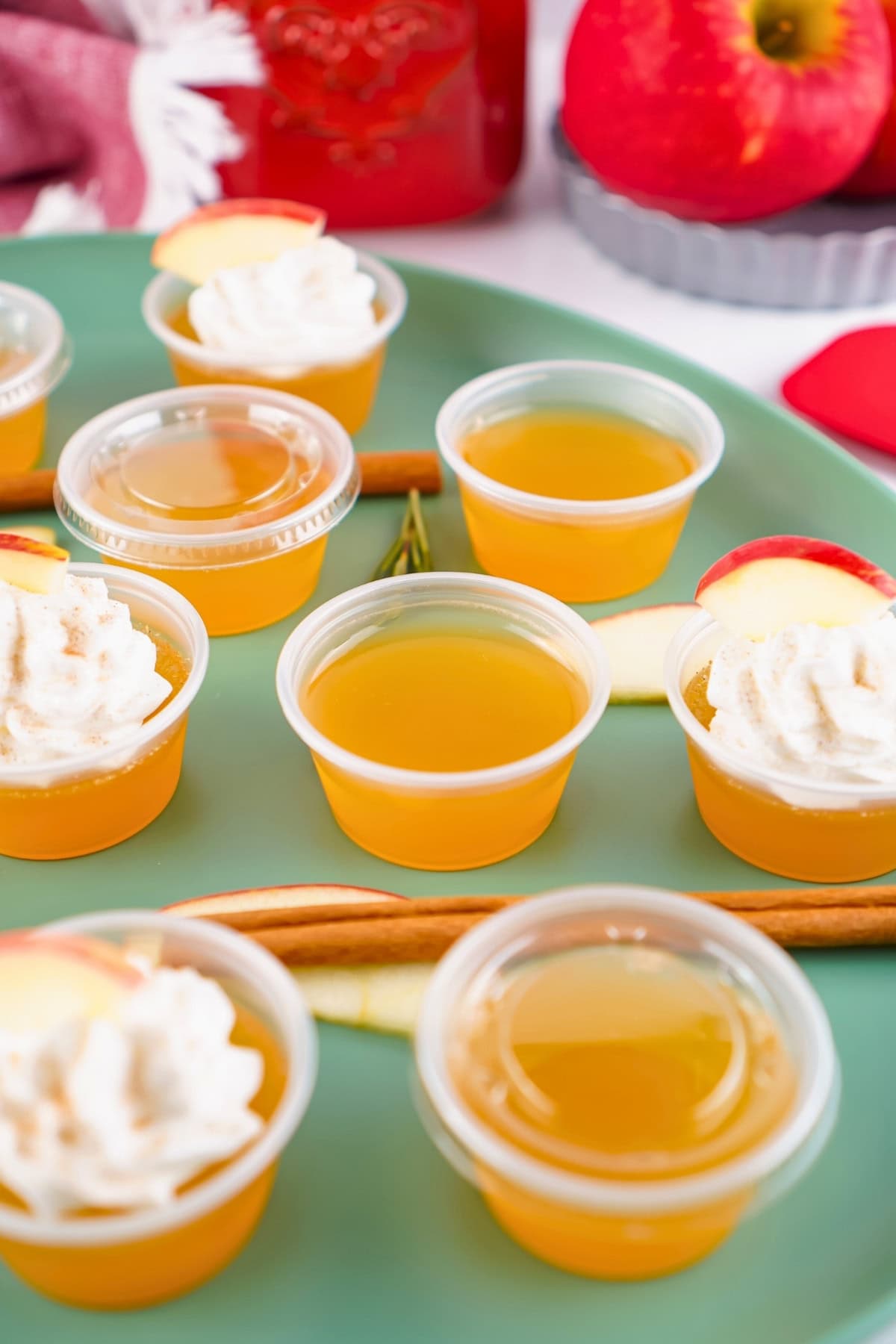 Small cups of yellow gelatin with whipped cream and apple slices on a green plate.