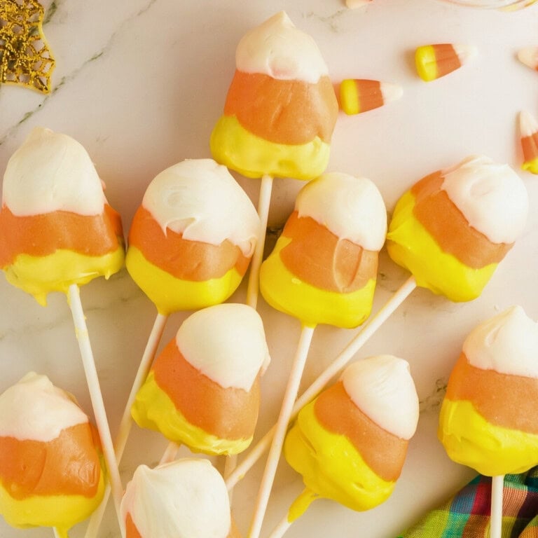 Cake pops decorated to look like candy corn, arranged on a marble surface.