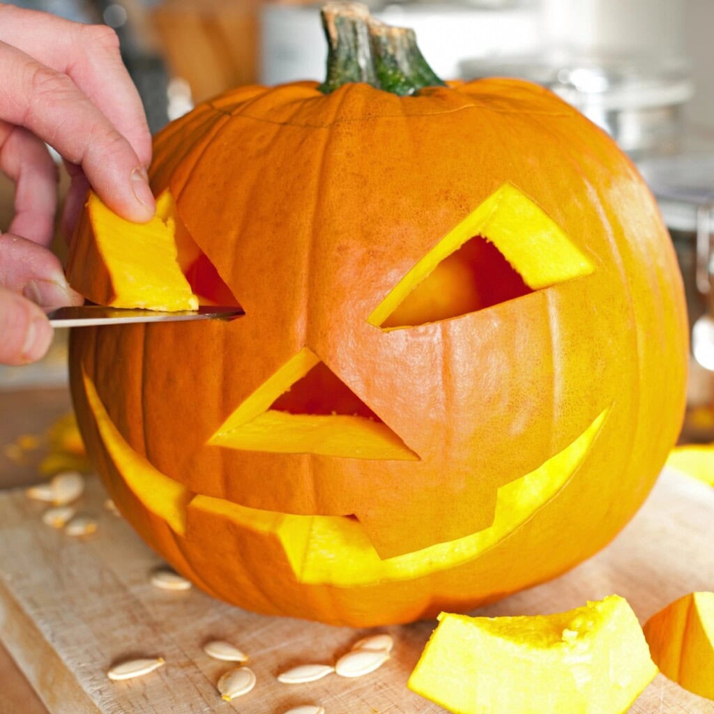 A hand carving a smiling jack-o-lantern, learn how to preserve carved pumpkins.