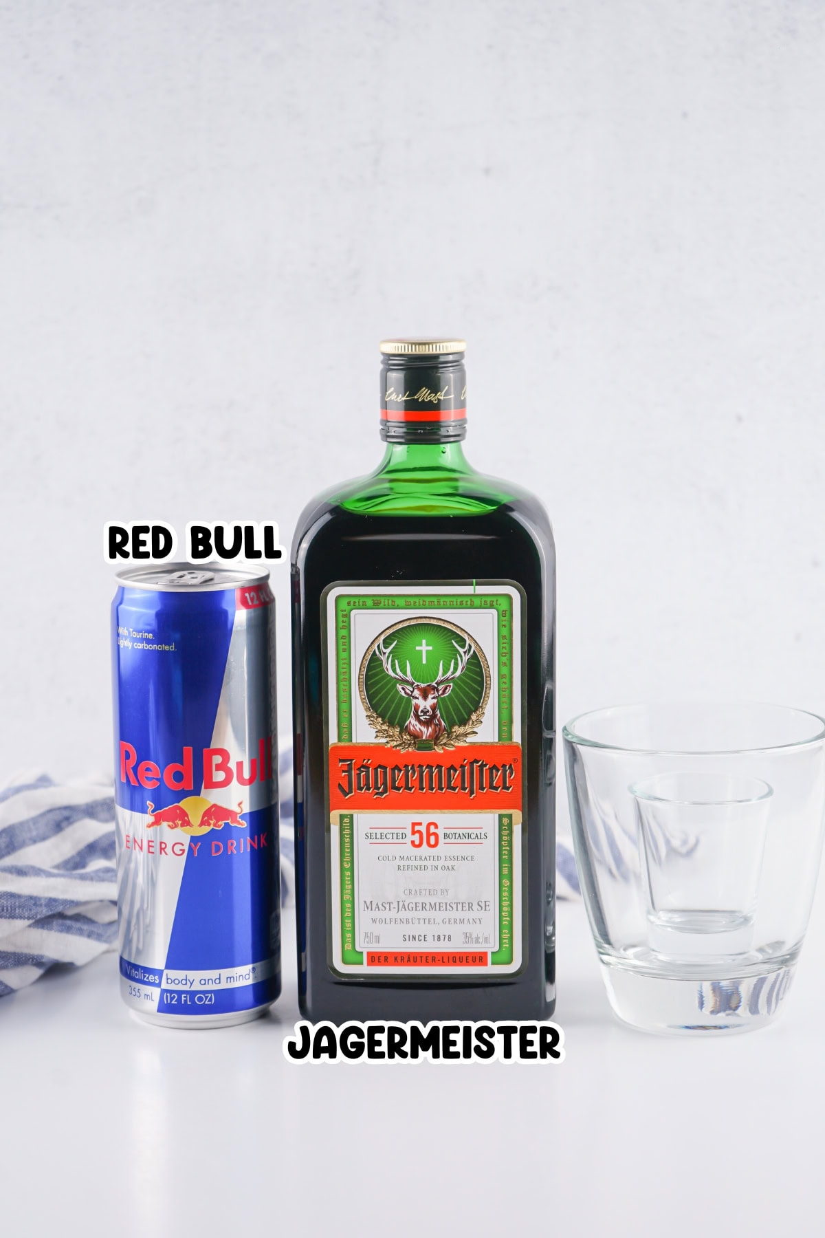 A can of Red Bull, a bottle of J&auml;germeister, and an empty glass on a table.