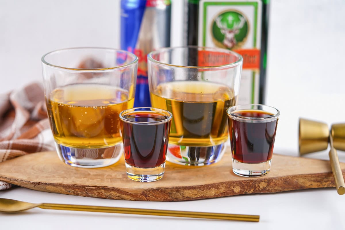 Two short glasses and two shot glasses with dark drinks on a wooden board.