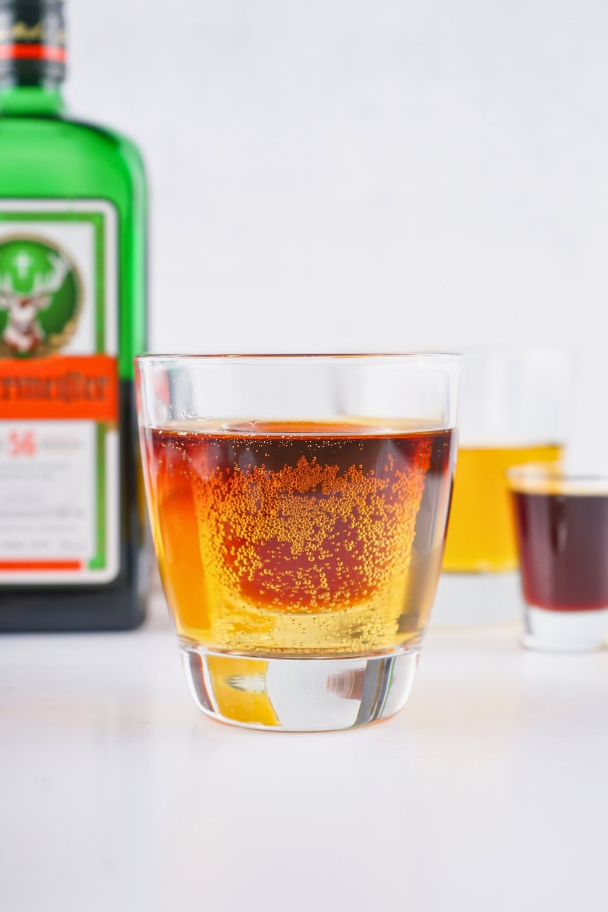A glass of amber cocktail with a green liqueur bottle in the background.