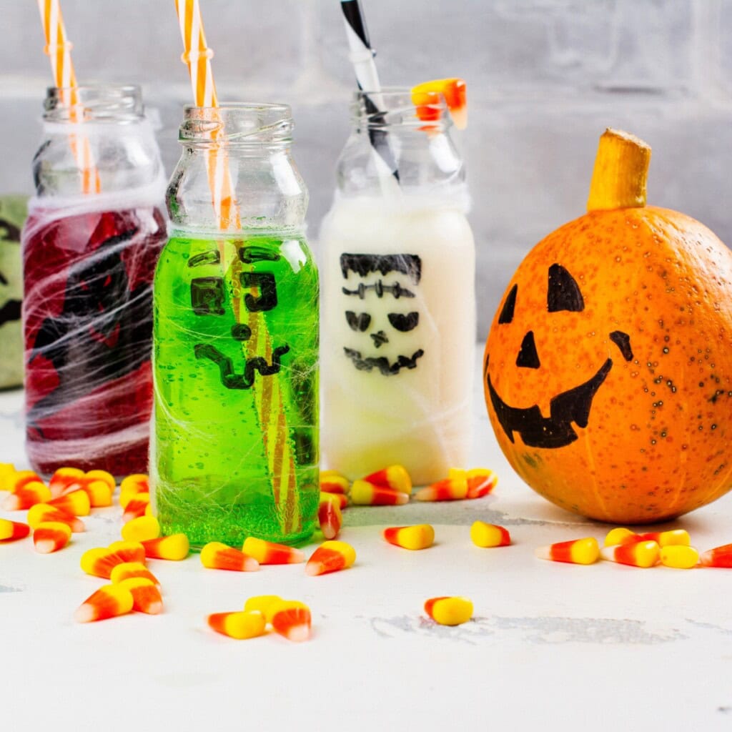 Three Halloween mocktails and a jack-o-lantern pumpkin with candy corn.
