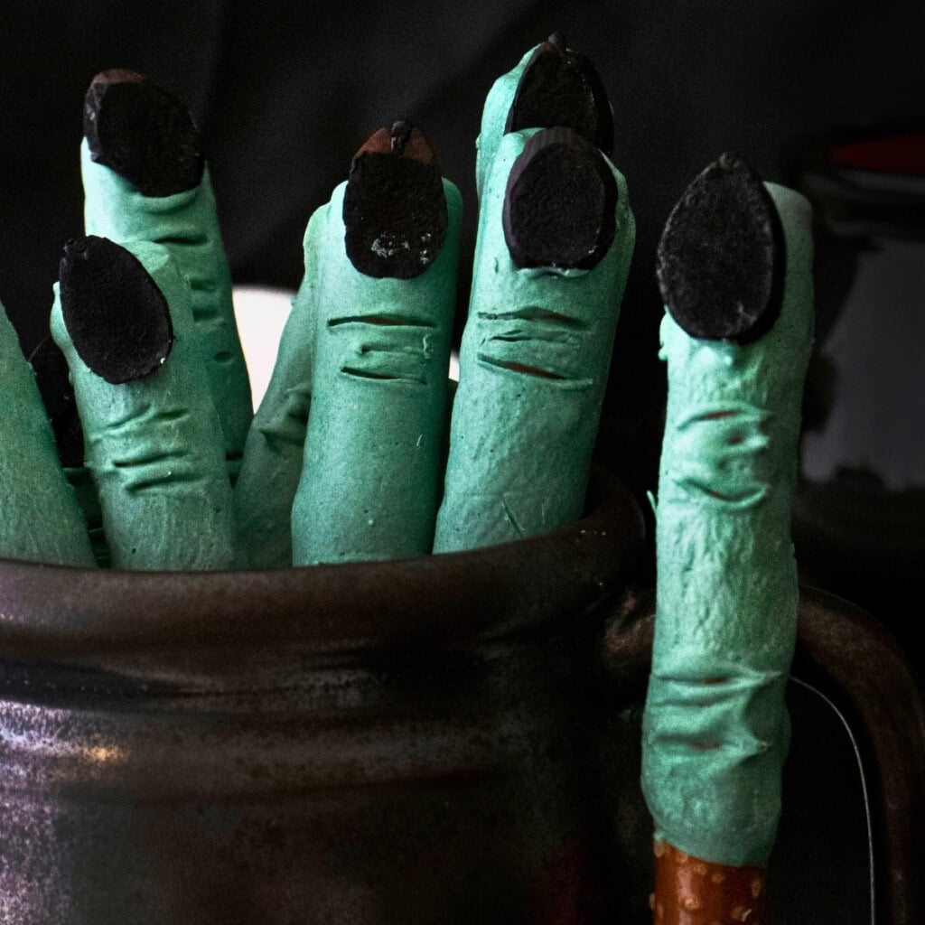 Savory Halloween food: Green witch finger cookies with black nails in a black mug.