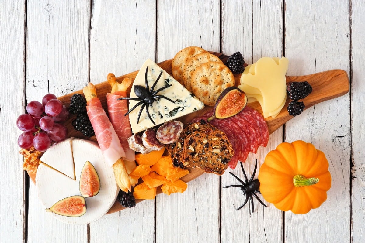 Halloween-themed charcuterie board with cheese, meats, fruit, and fake spiders.
