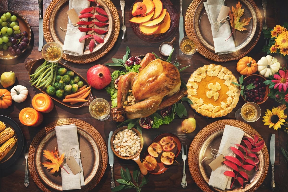 Thanksgiving dinner table with roast turkey, pie, vegetables, and autumn decor.