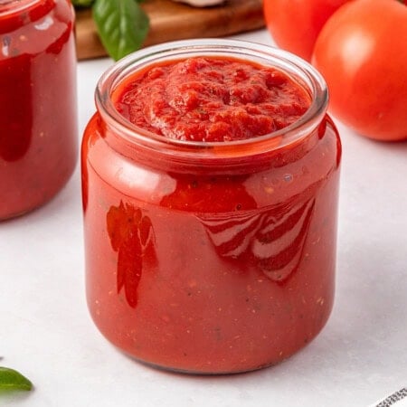 A glass jar filled with thick red tomato sauce on a white surface.