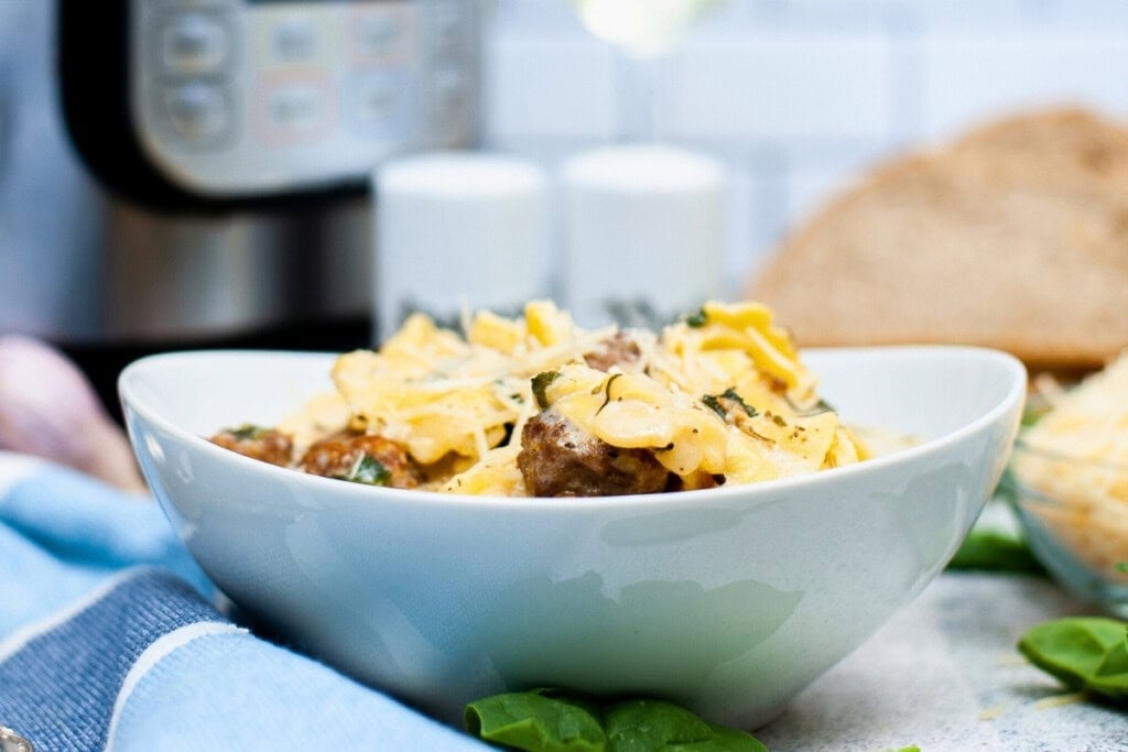 A bowl of pasta with meatballs and herbs, topped with grated cheese.