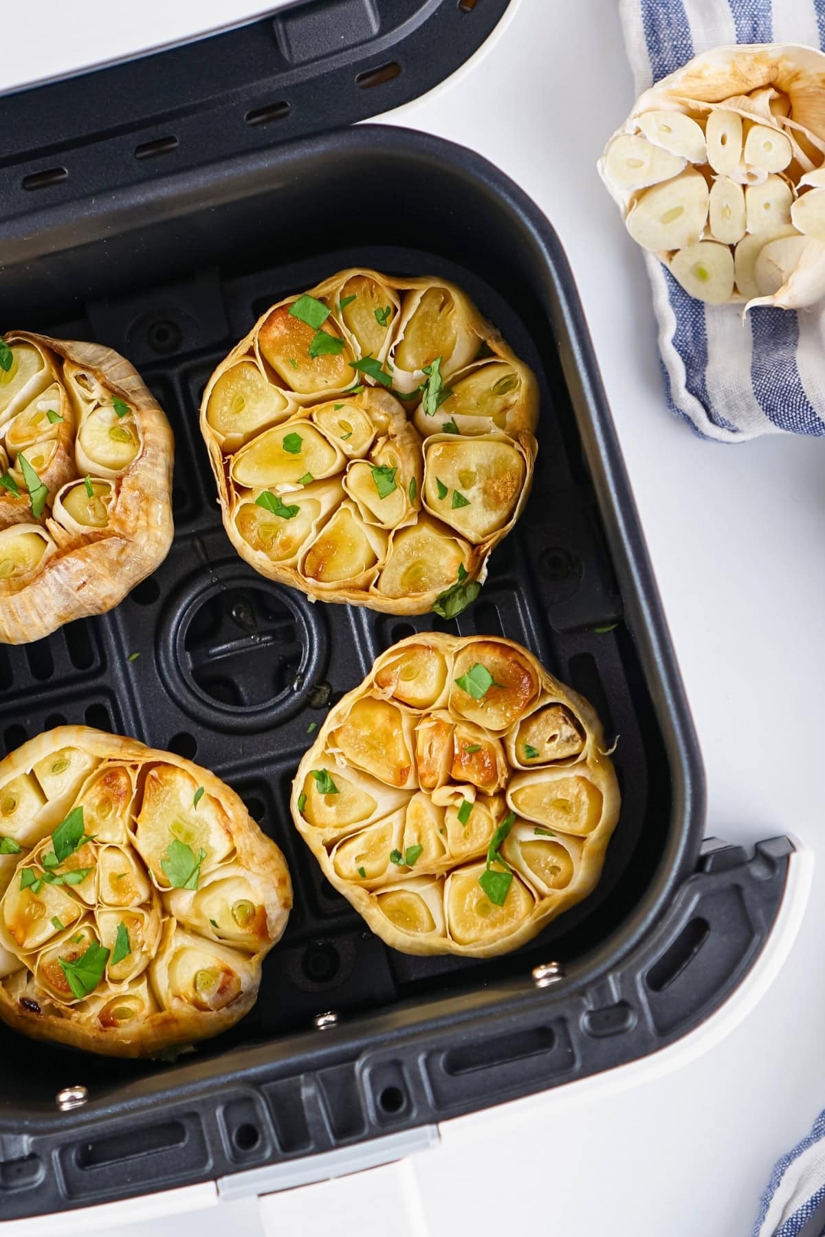Four roasted garlic bulbs in an air fryer basket, garnished with chopped parsley.