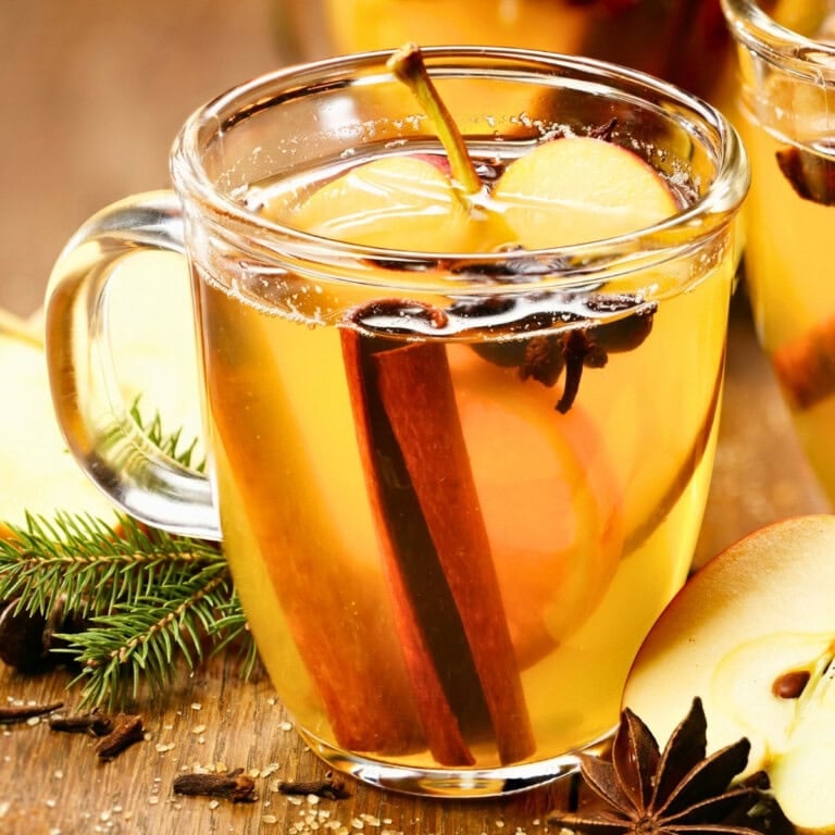 Clear glass mug of spiced apple cider, a cozy choice for Thanksgiving mocktails.