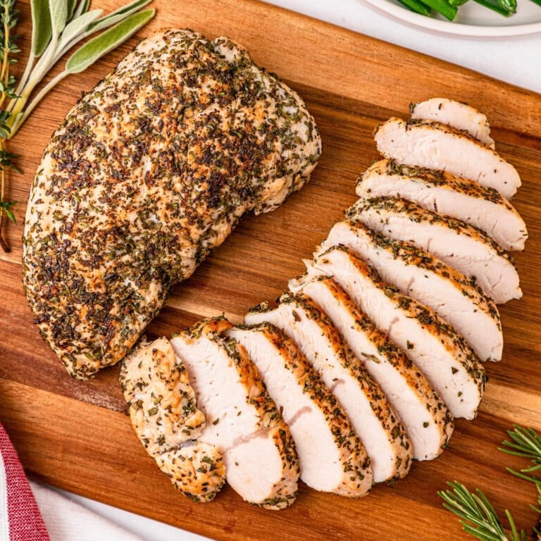 Sliced herb-crusted turkey breast on a wooden cutting board.