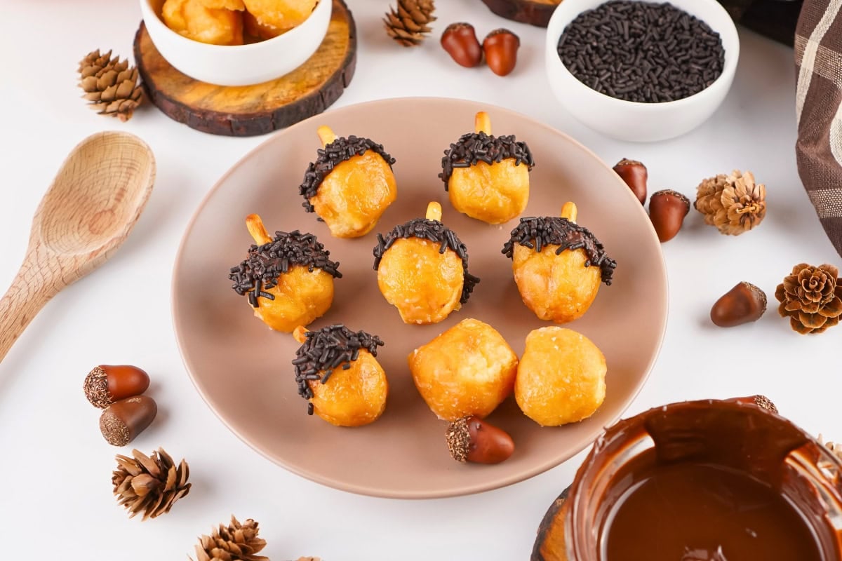 Plate of acorn-shaped donut holes with chocolate sprinkles on a table.