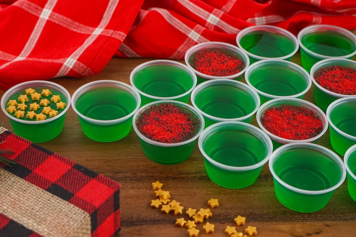 Small cups of green gelatin, some topped with festive red or yellow sprinkles.