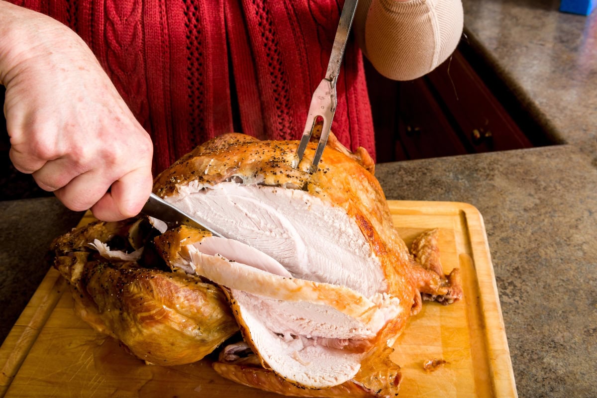 Person carving a roasted turkey breast on a cutting board in a kitchen.