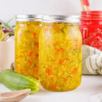 Two jars of homemade sweet relish with chopped vegetables and a fresh cucumber.