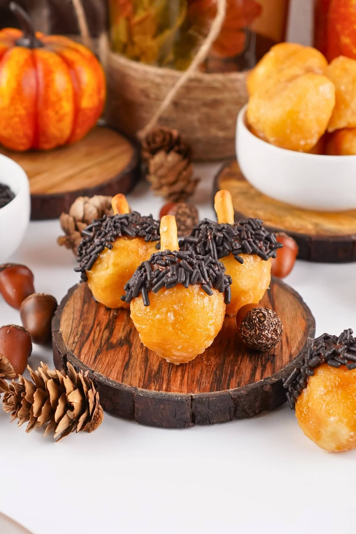 Three acorn-shaped treats with chocolate sprinkles on a wooden slice, autumn decor.
