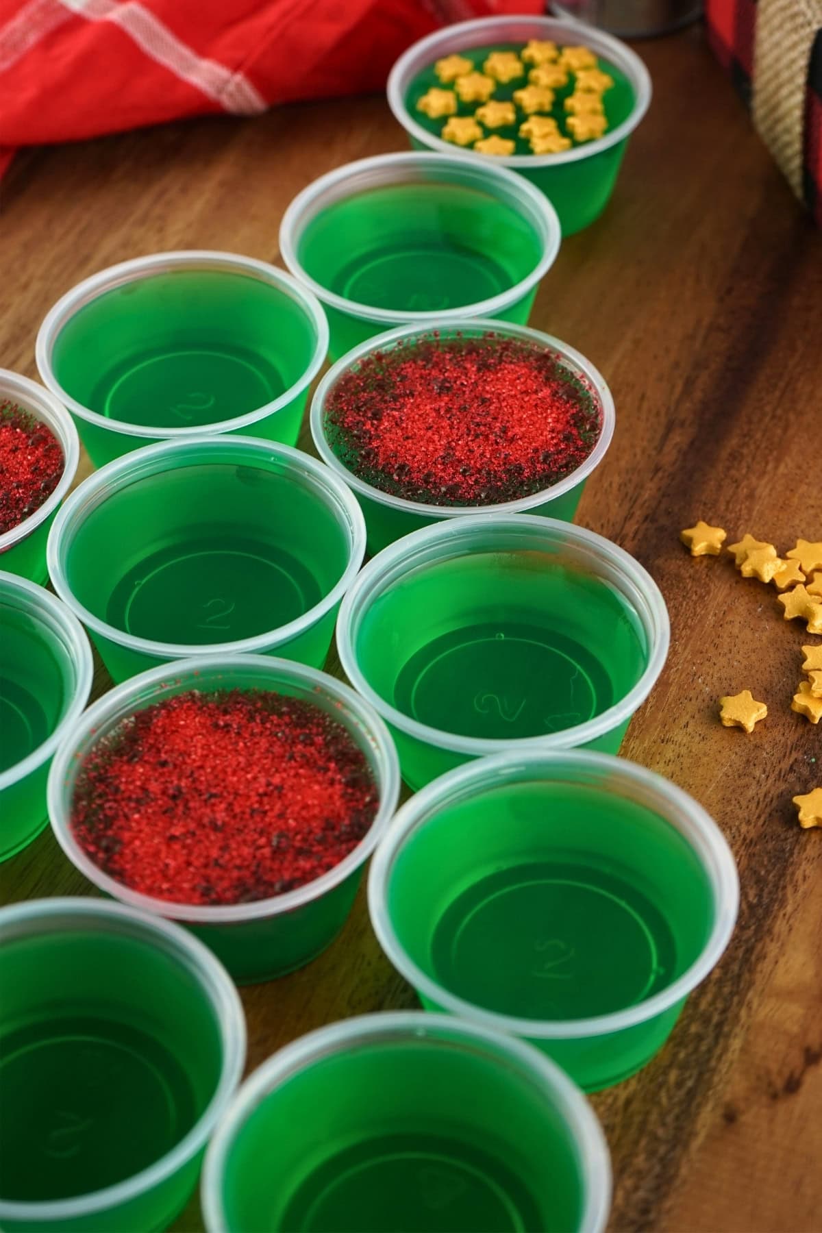 Green gelatin cups, some topped with red sprinkles or yellow star-shaped sprinkles.