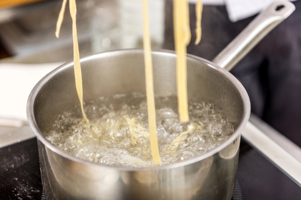 Long pasta is being boiled in a pot of water on a stovetop.