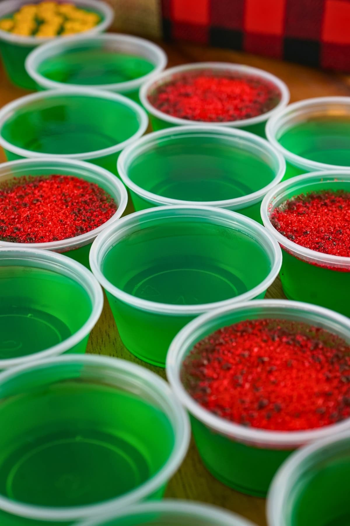 Small plastic cups filled with green gelatin, some topped with red sprinkles.