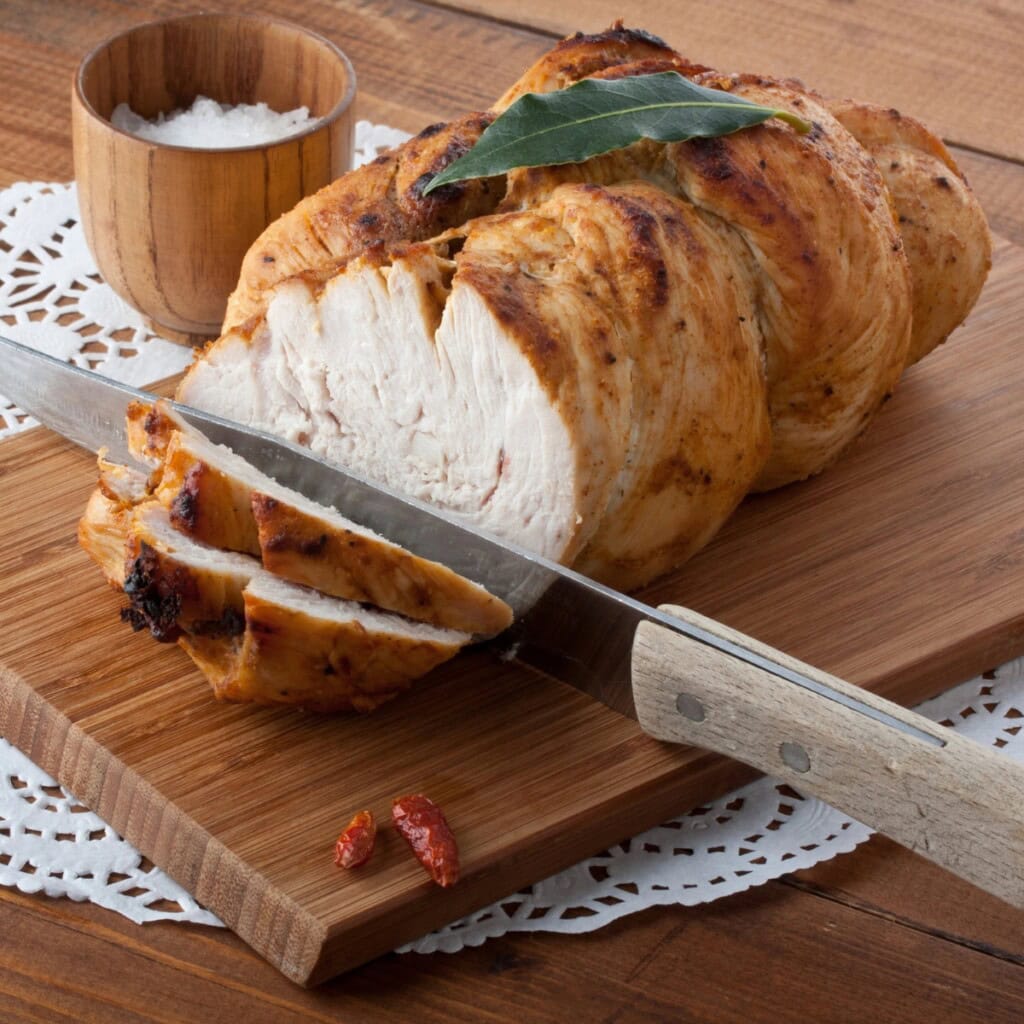 Carve a turkey breast on a wooden board with salt and a knife nearby.