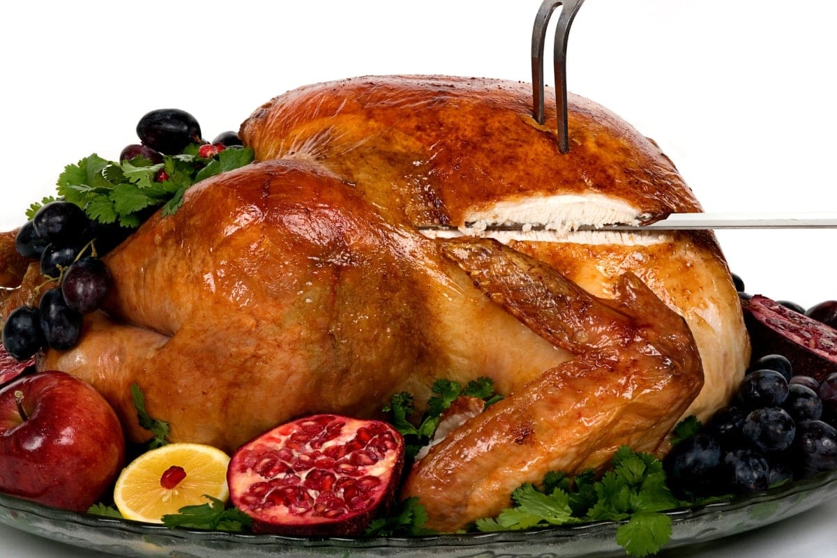 Roast turkey being carved, surrounded by fruits and greens on a platter.