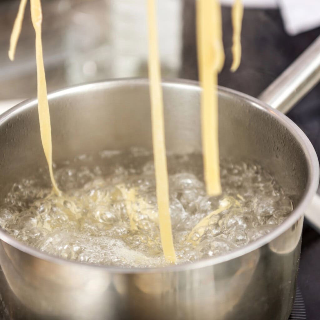Fresh pasta noodles being dropped into a pot of boiling water on the stove.