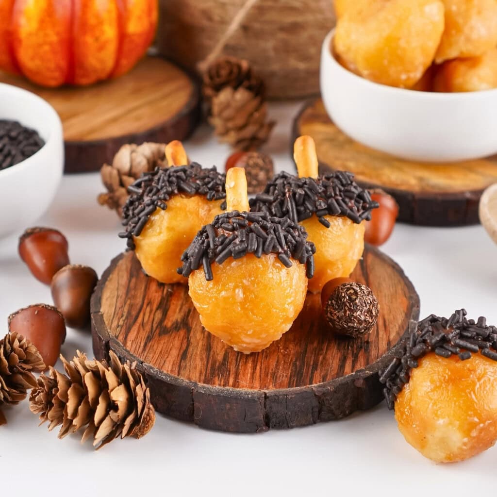 Three chocolate Donut Holes shaped like acorns with sprinkles and pretzel stems.