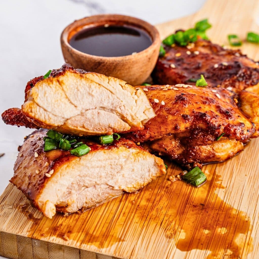 Grilled chicken breast with sauce and green onions on a wooden board.