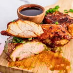 Grilled chicken breast with sauce and green onions on a wooden board.