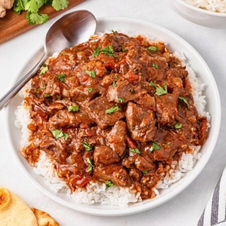 A bowl of curry beef stew served over white rice, garnished with fresh herbs.