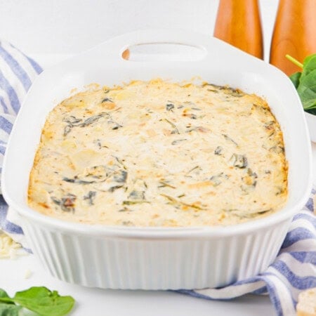 Creamy spinach artichoke dip in a white baking dish on a striped towel.