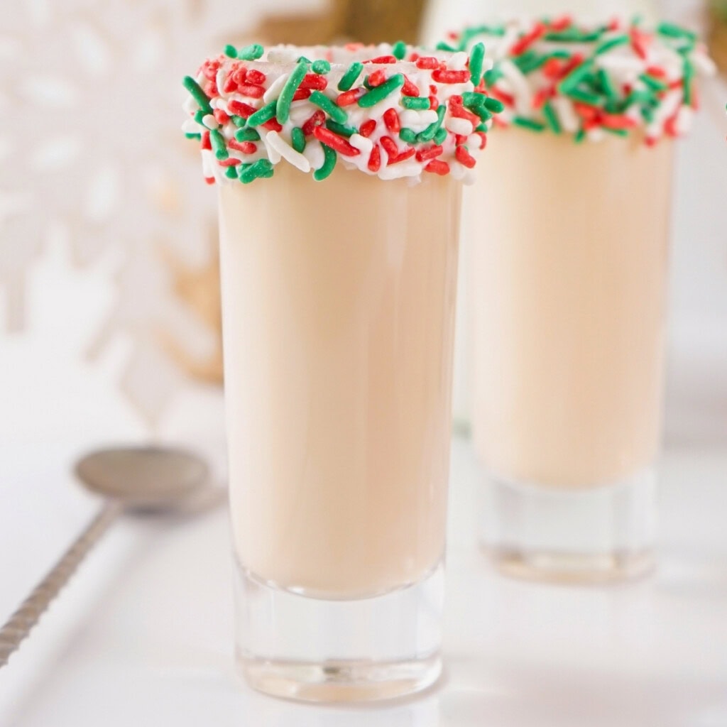 Creamy holiday shot with red and green sprinkles on the rim in a clear glass.