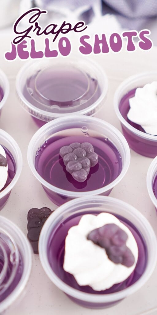 Plastic cups of purple grape jello shots, some topped with whipped cream and gummies.