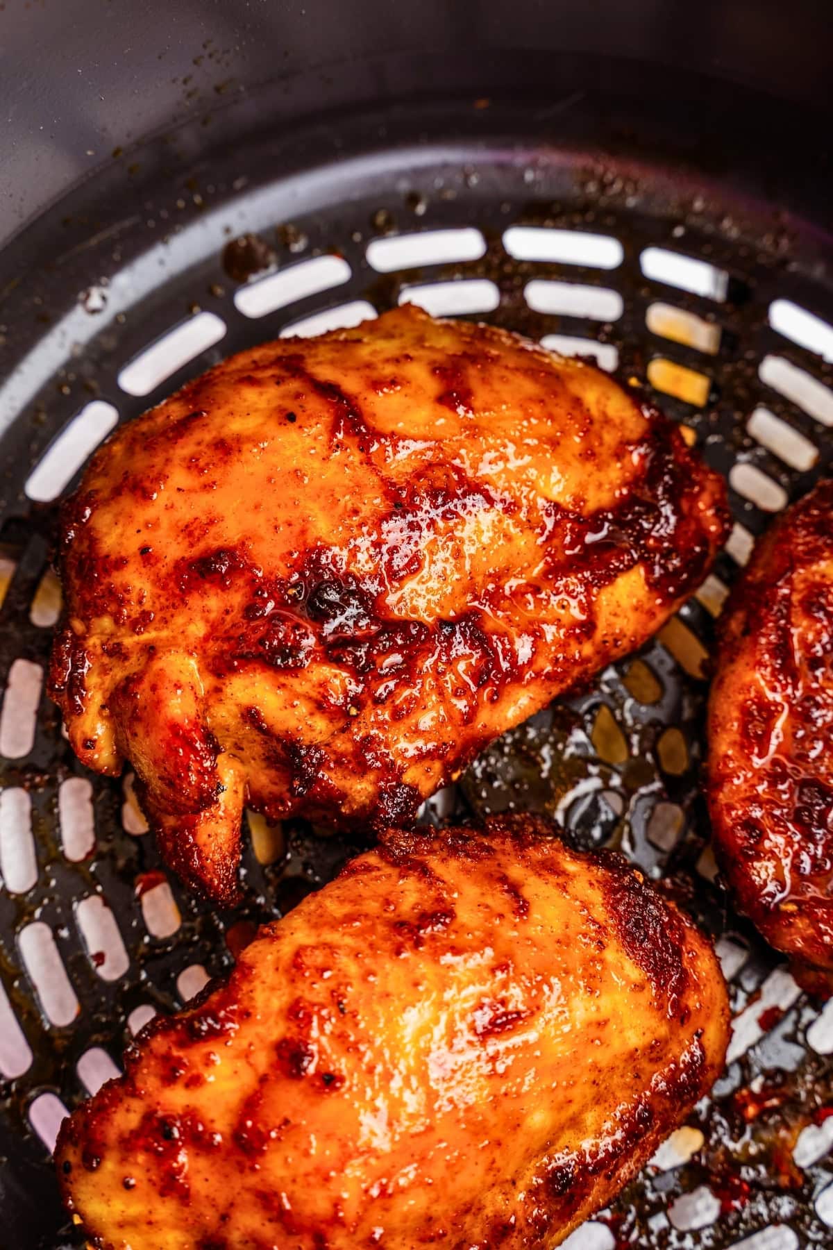 Three pieces of seasoned chicken cooking in an air fryer basket.