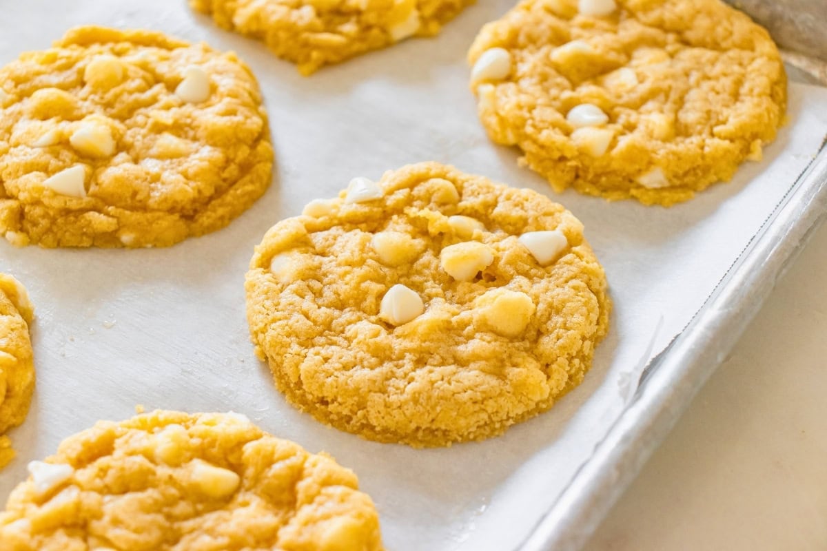 Cookies with white chocolate chips on a parchment-lined baking sheet.