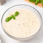 Creamy bechamel sauce in a glass bowl, topped with fresh basil leaves.
