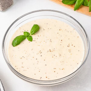 Creamy bechamel sauce in a glass bowl, topped with fresh basil leaves.