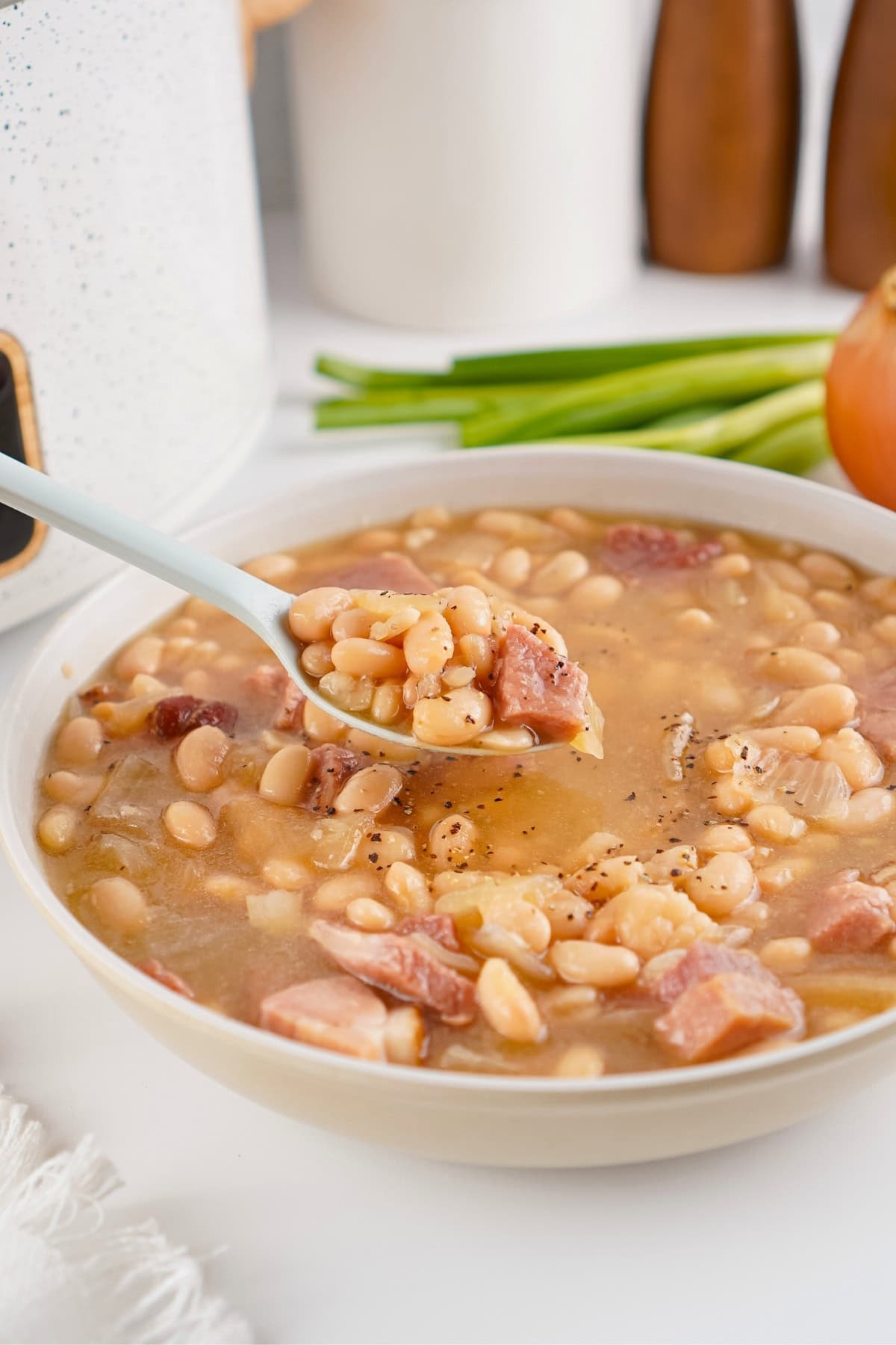 A bowl of bean soup with ham, with a spoon lifting a portion.